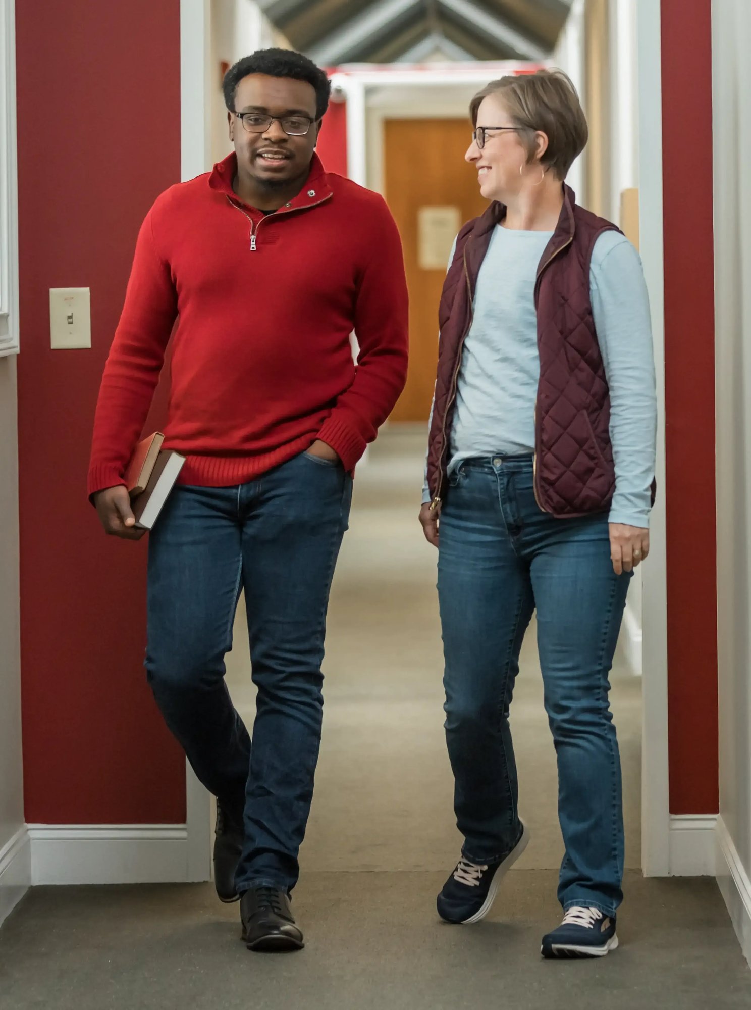 Two seminary students walking and talking in an Atlanta campus hallway with one carrying a book
