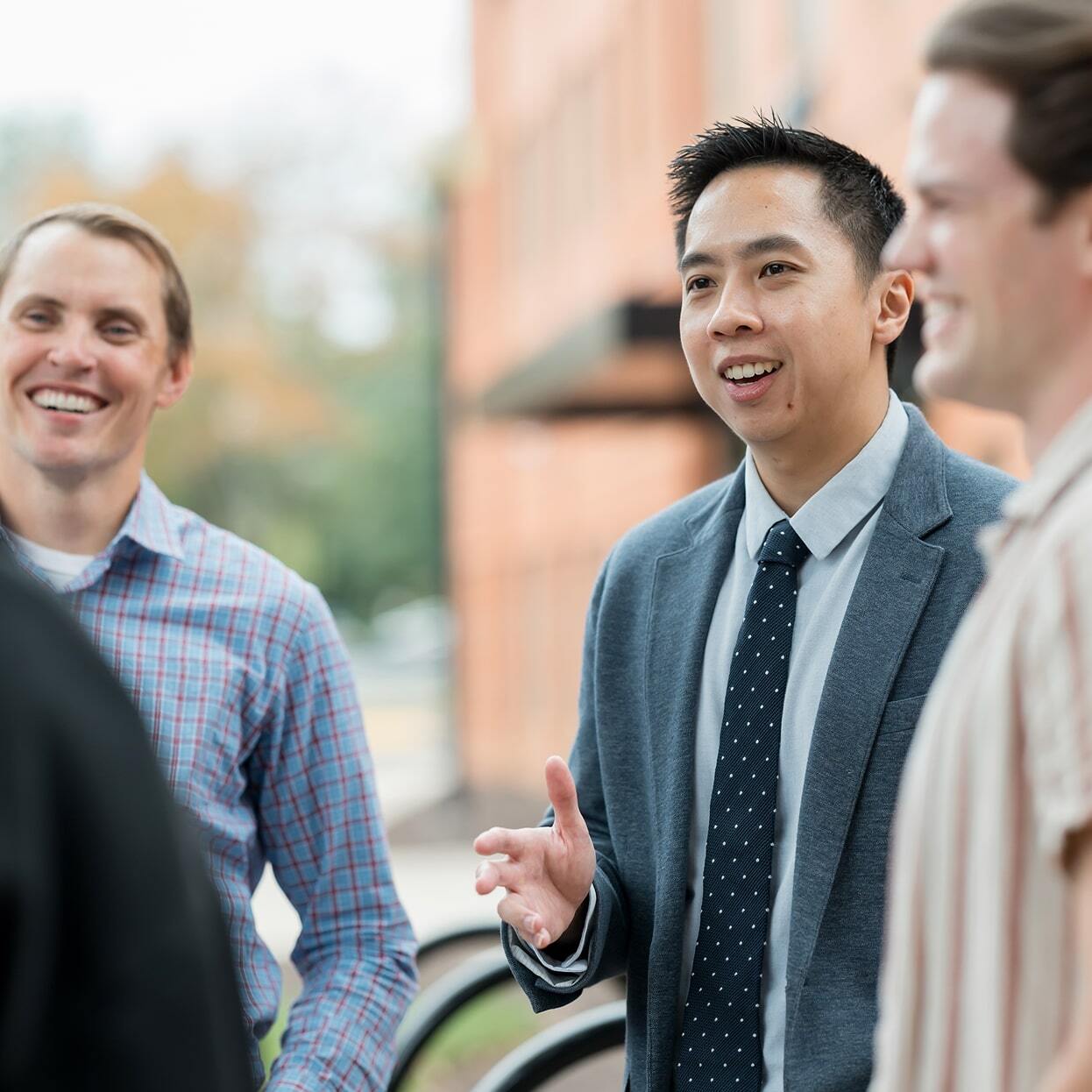 Group of men standing outdoors on campus engaged in a friendly conversation.