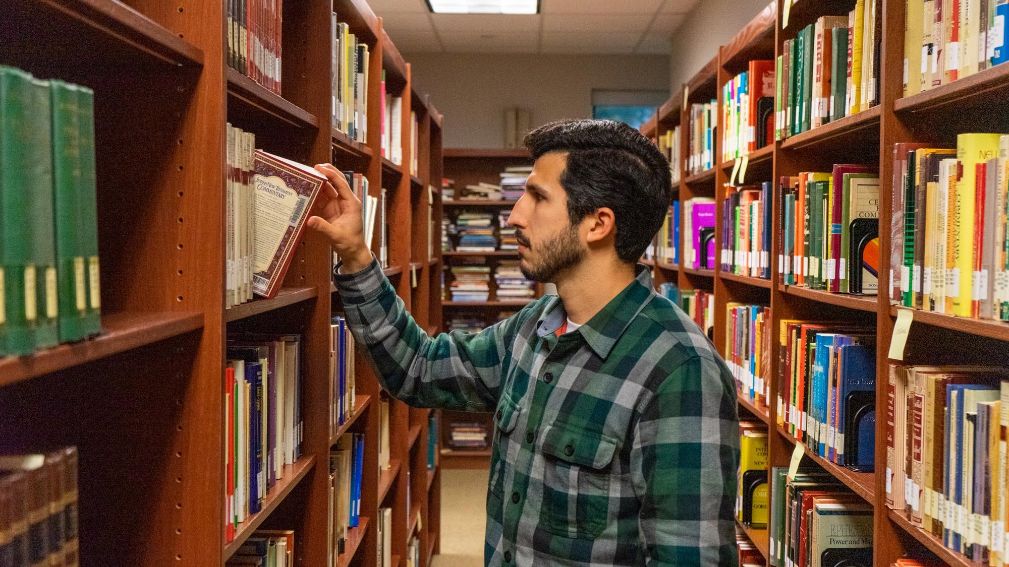 Student browsing books on library shelves in an indoor library aisle