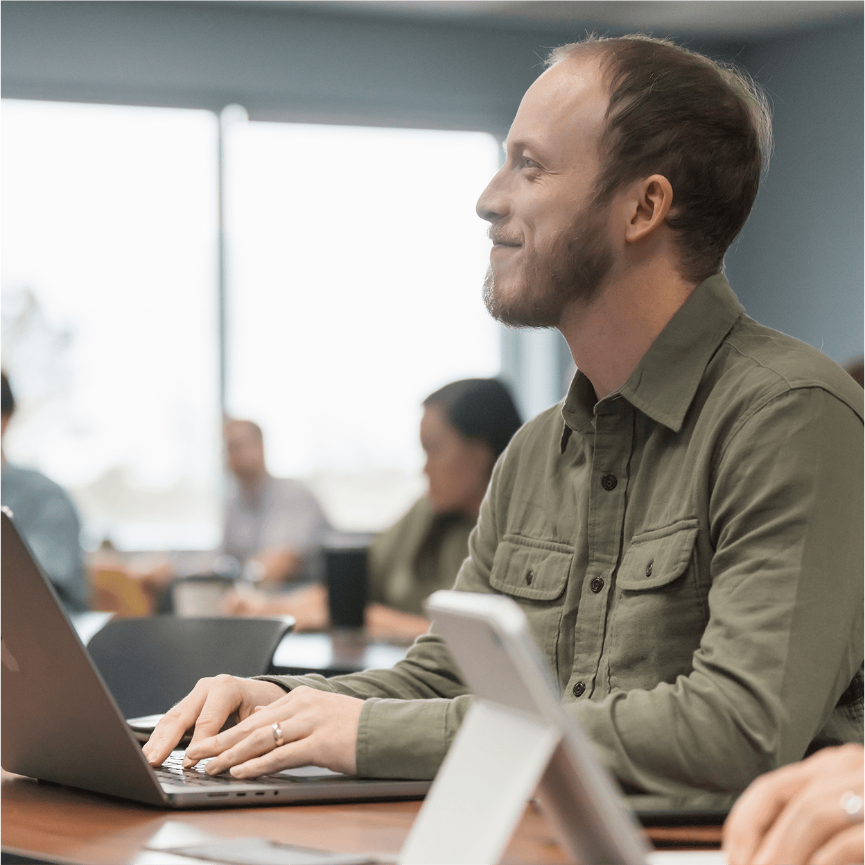 Man smiling typing on a macbook in class