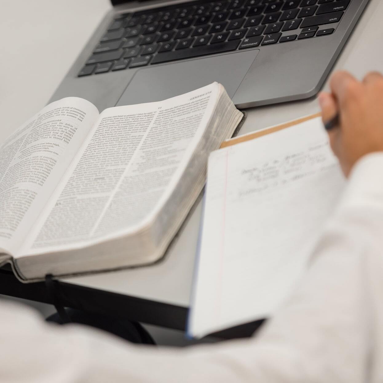 Open Bible on a desk next to a laptop and handwritten notes as a student studies Scripture