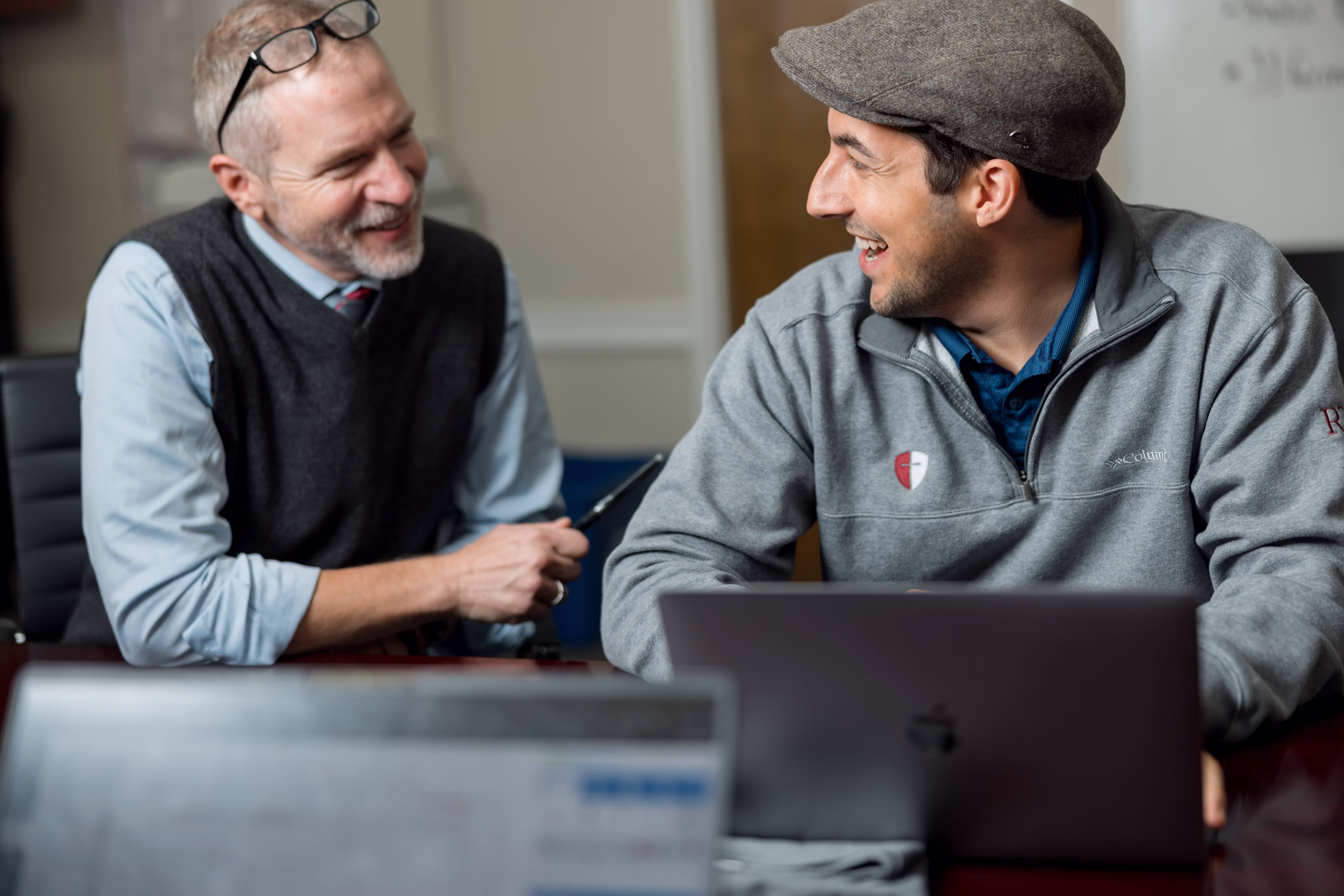 Mentor and student talking together indoors while sitting at a table with a laptop